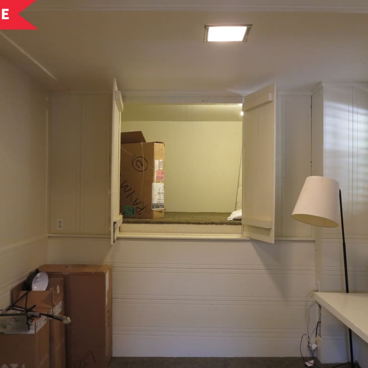 Small room with boxes, a floor lamp, and a desk, featuring a raised platform with open shutters.