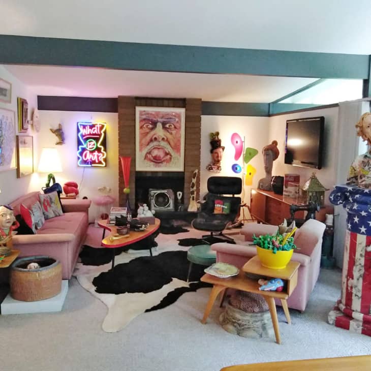 Eclectic living room with pink sofas, neon art, cowhide rug, and various sculptures, including a statue draped in an American flag.