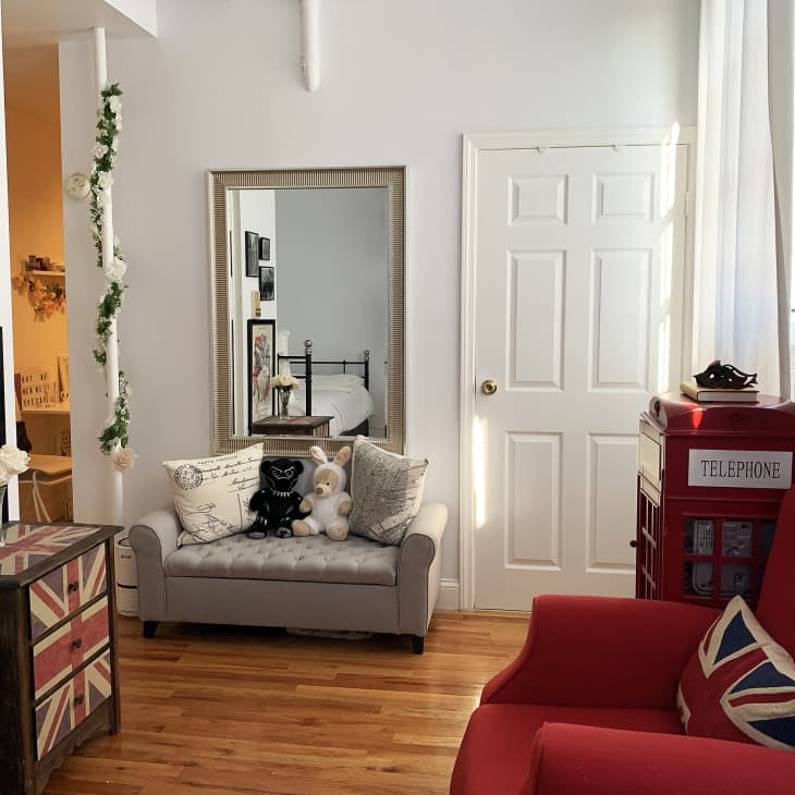 Cozy room with red armchair, Union Jack pillow, gray loveseat, large mirror, and red telephone booth decor.