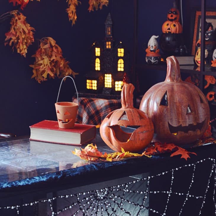 Halloween-themed room with carved pumpkins, autumn leaves, a lit candle, and a decorative haunted house on a table.