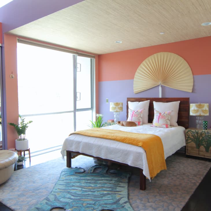 Colorful bedroom with a fan-shaped wall decor, bed with yellow throw, patterned pillows, and a small dog.