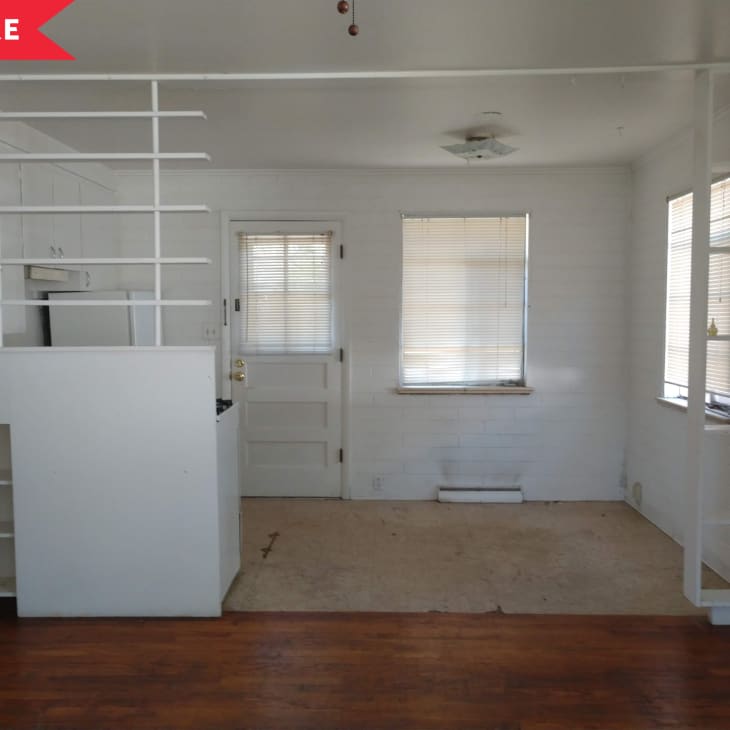 Small room with white walls, built-in shelves, and a door with blinds. Brown wooden floor and beige carpet area.