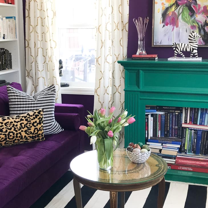 Living room with purple sofa, leopard print pillow, green fireplace, bookshelves, and a round table with tulips.
