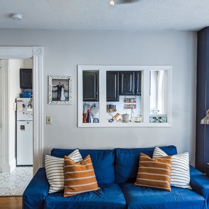 Blue sofa with striped pillows in living room, view into kitchen with dark cabinets, framed photo on wall.
