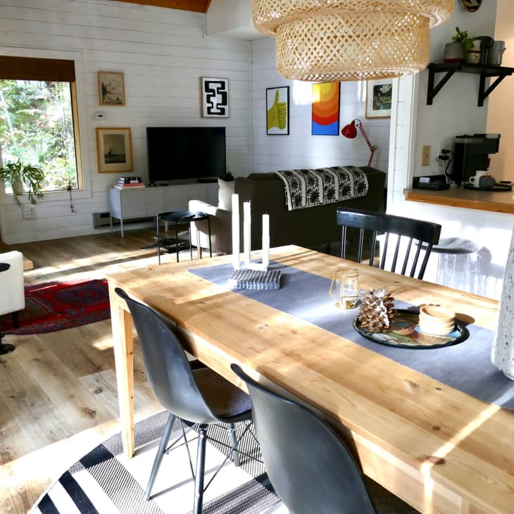 Open-plan living and dining area with wooden table, black chairs, large vase, wicker light fixture, and cozy seating area.