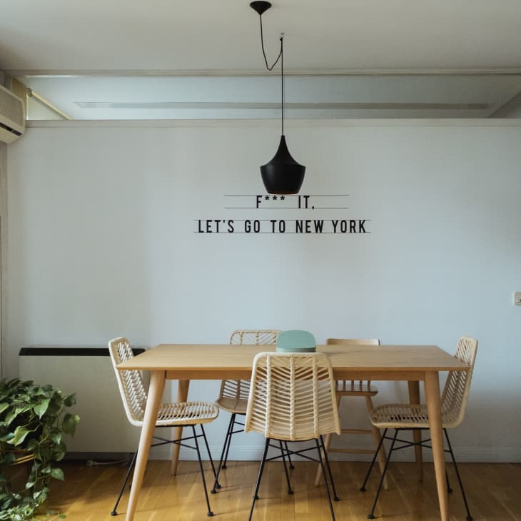 Dining room with wooden table, wicker chairs, black pendant light, and wall text "Let's go to New York."