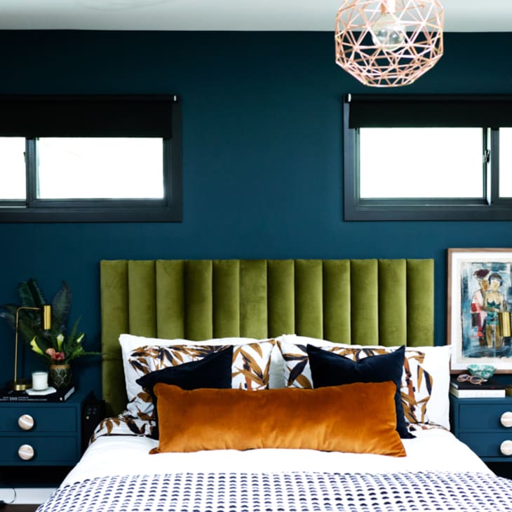 A blue bedroom with a green velvet headboard.