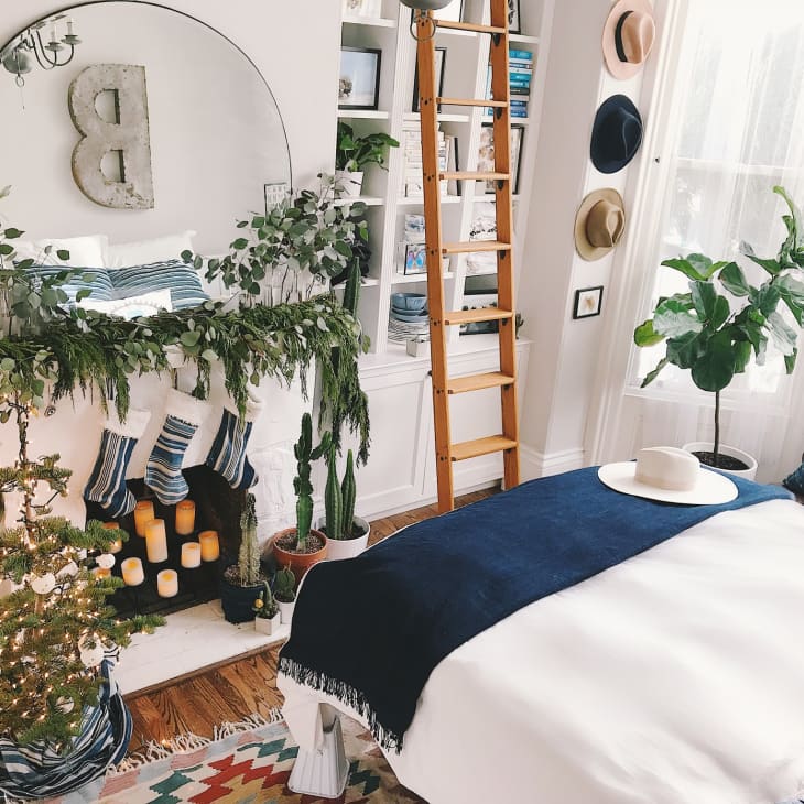 Cozy bedroom with a decorated fireplace, candles, greenery, a wooden ladder, and a bed with blue and white bedding.