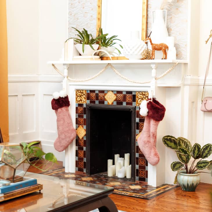 Living room with a decorated fireplace, pink stockings, plants, and a blue sofa.