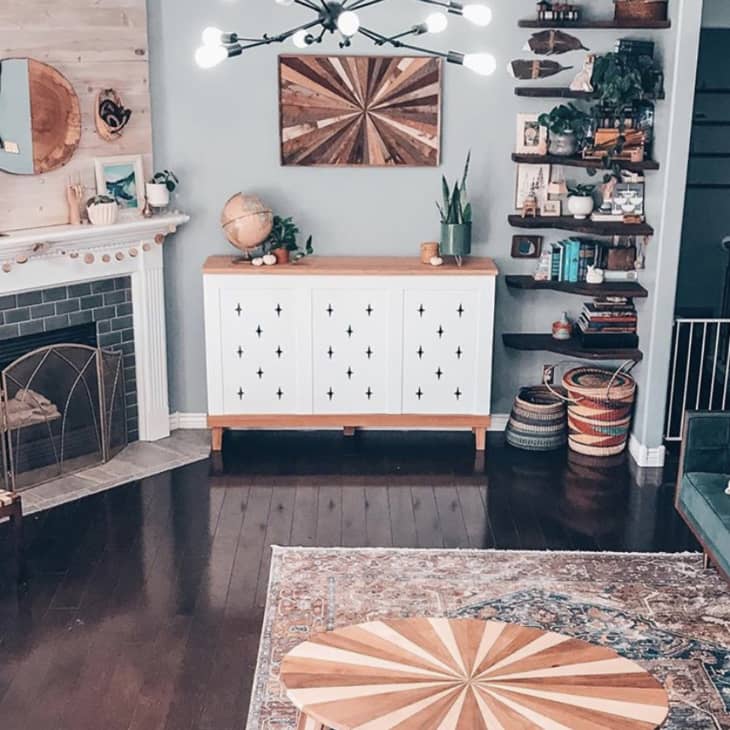 Living room with a fireplace, modern chandelier, green sofa, wooden chairs, and a white cabinet with decorative items.