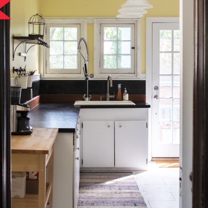Before: A classic kitchen with yellow walls, black countertops, white lower cabinets, and lots of windows