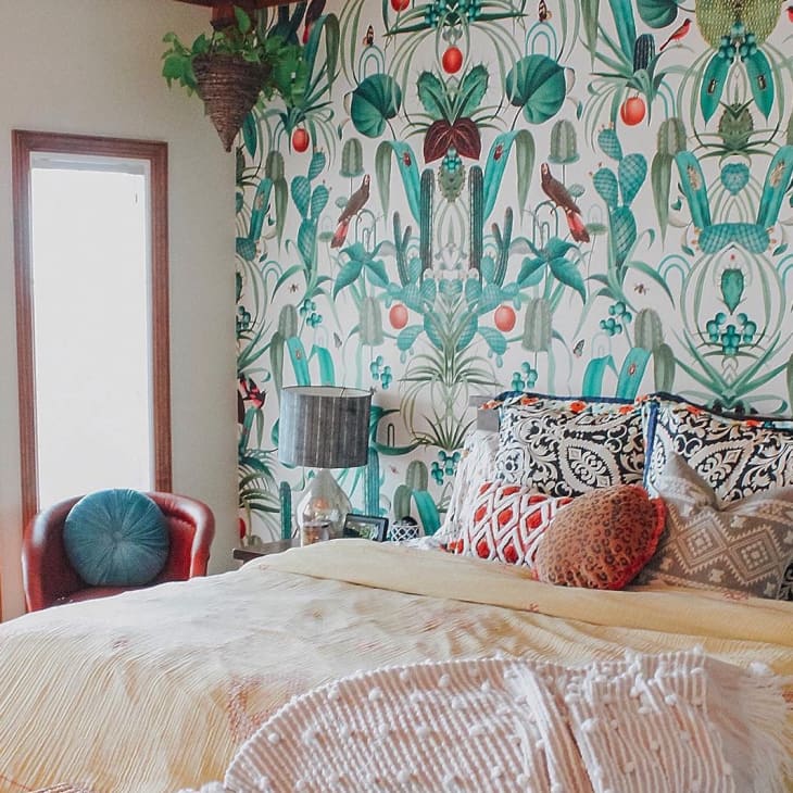 Bedroom with vibrant botanical wallpaper, patterned pillows, and a cozy bed with a yellow throw blanket.