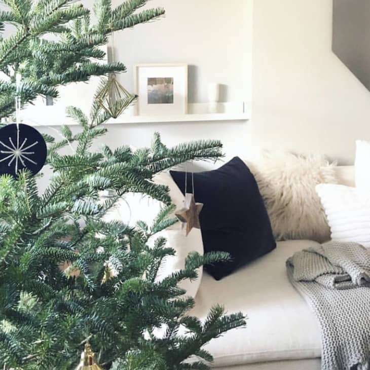 Christmas tree with geometric ornaments in a cozy living room with a white sofa, black and white pillows, and a gray throw.