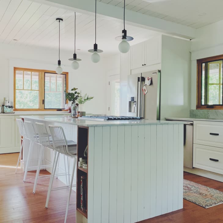 Modern kitchen with white cabinets, island with bar stools, pendant lights, and wooden floors.