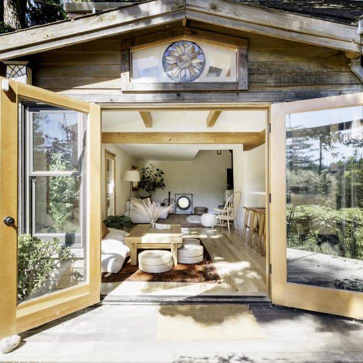 Open wooden doors leading to a cozy living room with white sofas, a wooden coffee table, and potted plants.