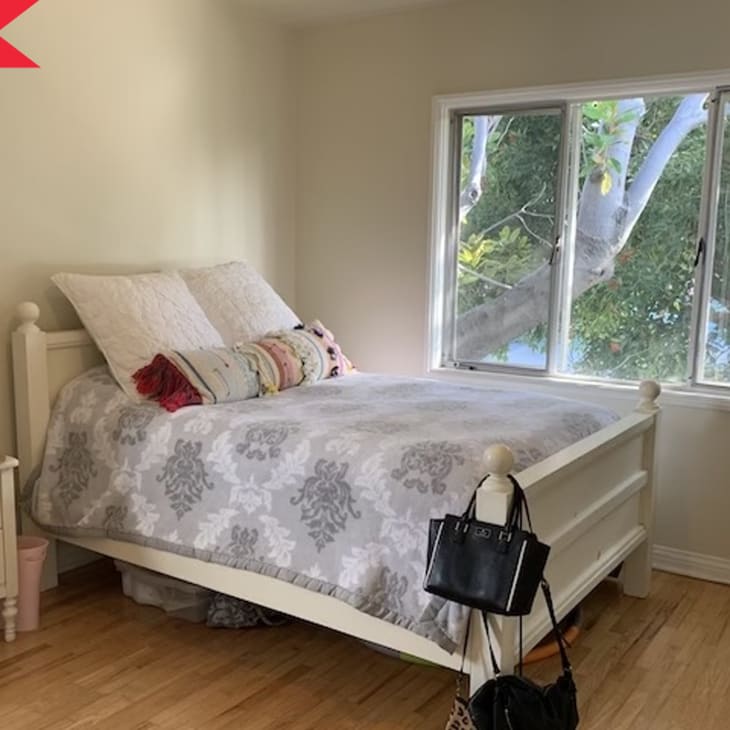 Bedroom with white bed, floral bedding, nightstand, lamp, and window view of trees.
