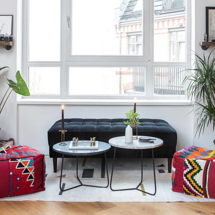 Cozy living room with red bean bags, black ottoman, chess set, plants, and decorative shelves by a large window.