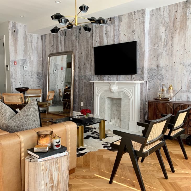 Living room with tan leather sofa, black chairs, large mirror, wall-mounted TV, and decorative fireplace.