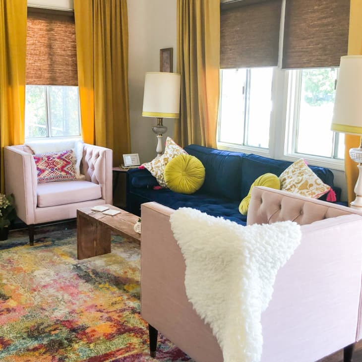 Living room with pink armchairs, blue sofa, yellow curtains, colorful rug, and decorative pillows.