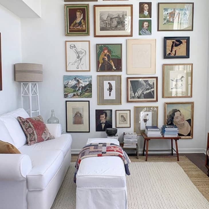 Living room with white sofa, gallery wall of framed art, and a large potted plant by the window.