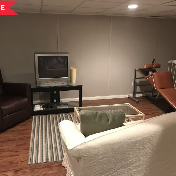 Basement room with brown recliner, TV on stand, exercise bench, and striped rug on wooden floor.