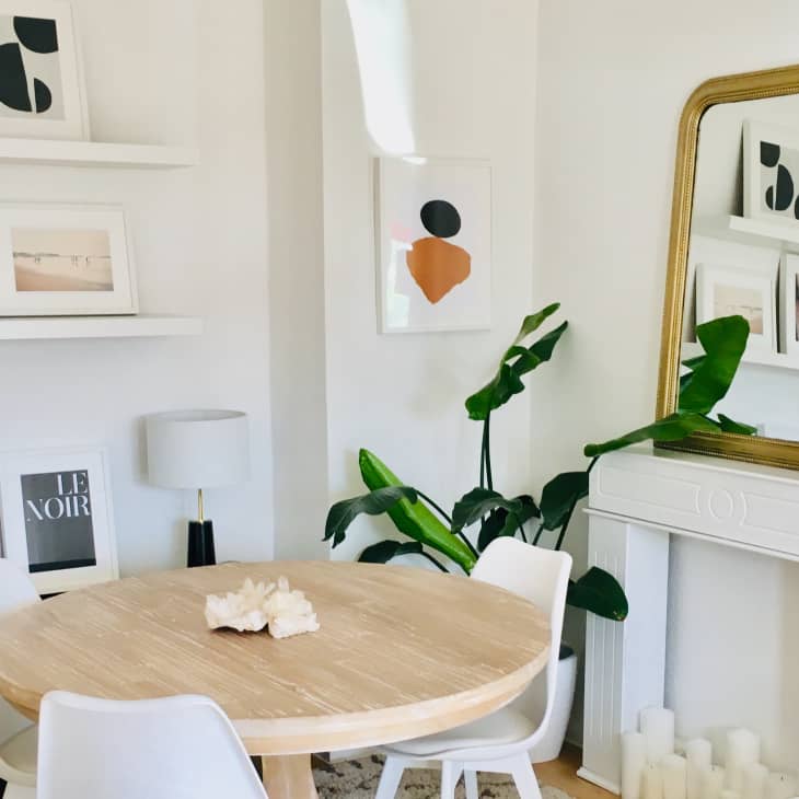 An arched mirror in a gold frame leaning on a white fireplace frame in a bright dining area