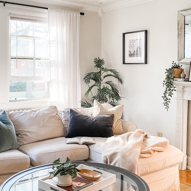 Cozy living room with a beige sectional sofa, green and black pillows, a round glass coffee table, and a decorated mantel.