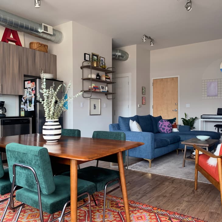 Open-plan living room with blue sofa, green chairs, wooden dining table, and a keyboard against the wall.