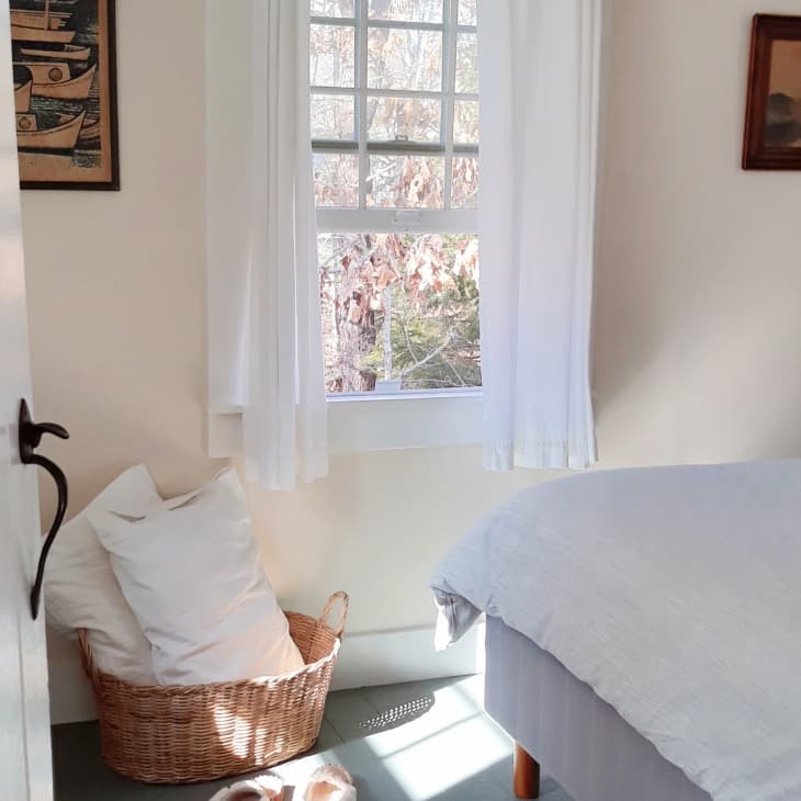Cozy bedroom with a wicker basket, white curtains, and framed art on the walls.