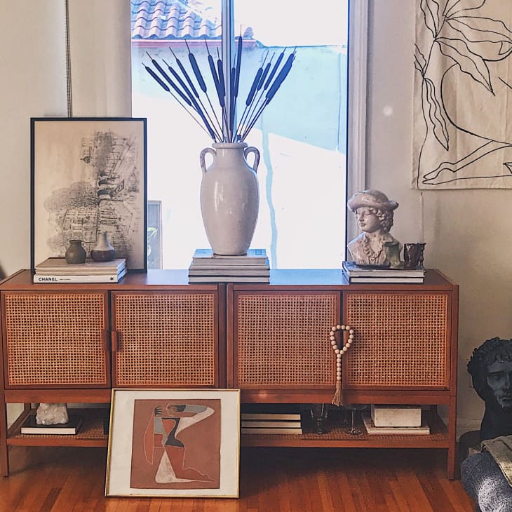 Mid-century modern sideboard with art, vases, and sculptures, flanked by mirrors and a woven wall hanging.