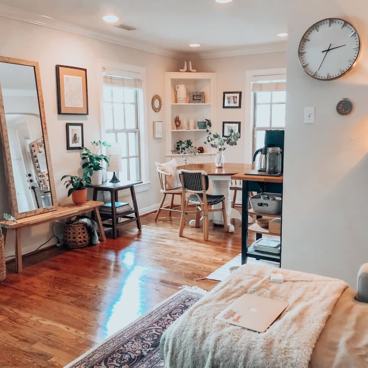 Cozy living room with wooden floors, a large mirror, plants, a round dining table, and a wall clock.