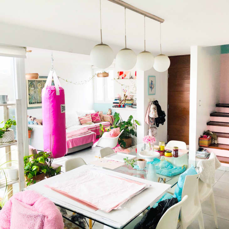 Bright living room with pink punching bag, plants, white chairs, and a glass dining table. Stairs lead to upper level.