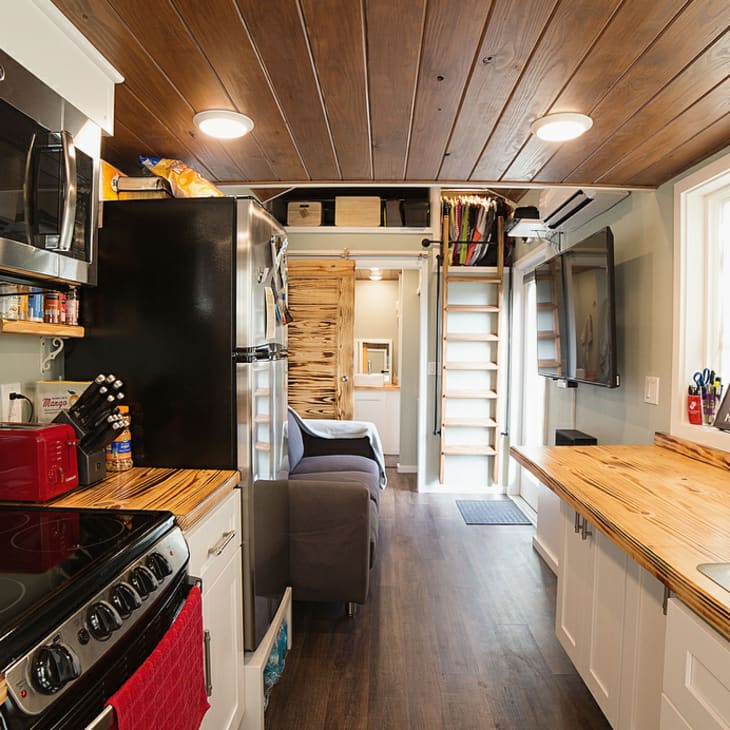 Tiny house kitchen with wood countertops, stainless steel appliances, red toaster, and a ladder leading to a loft.