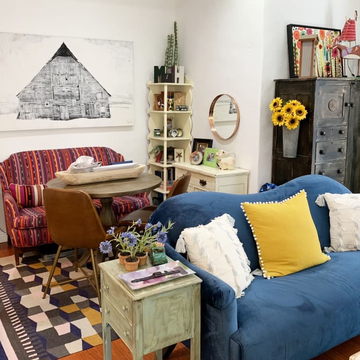 Cozy living room with blue sofa, yellow pillow, striped loveseat, rustic decor, and a barn painting on the wall.