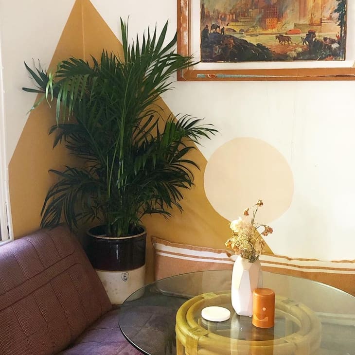 Cozy corner with a purple sofa, glass table, potted plant, and framed landscape painting.