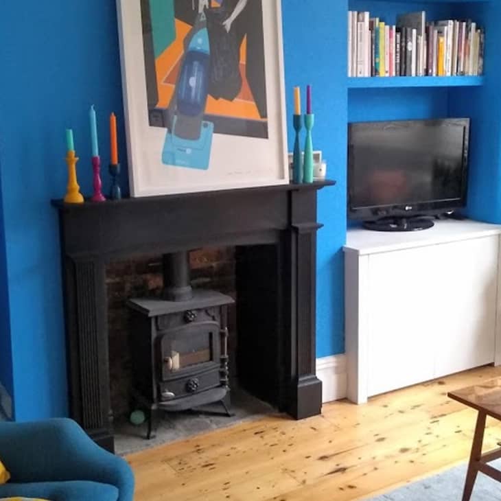 Living room with blue walls, black fireplace, colorful candles, TV on white cabinet, and plants on wooden floor.