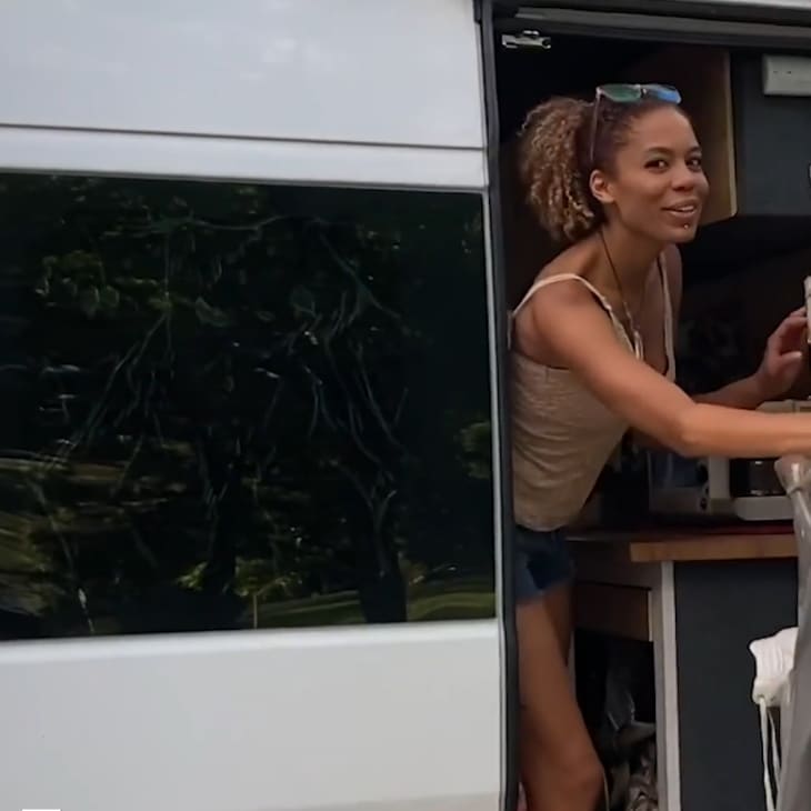 Woman smiling while stepping out of a white camper van with open doors.