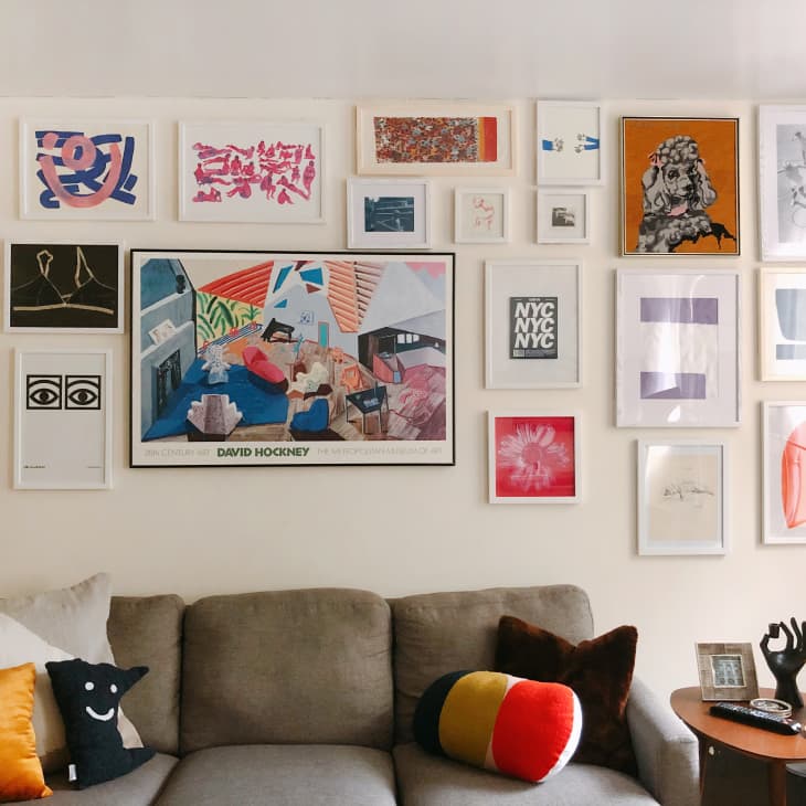 Gallery wall with colorful art above a beige sofa, featuring eclectic pillows and a small side table with decor items.