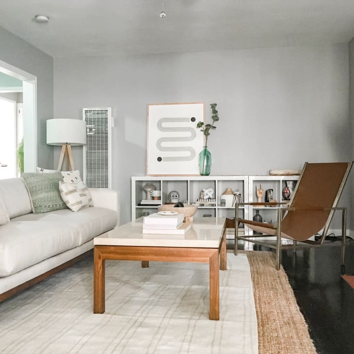 Modern living room with a beige sofa, wooden coffee table, abstract art, and a brown chair on a layered rug.