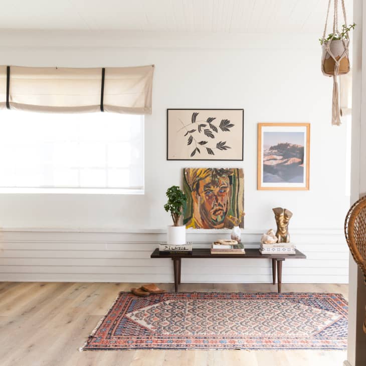 Living room with a patterned rug, wall art, a wooden bench, potted plant, and decorative items.