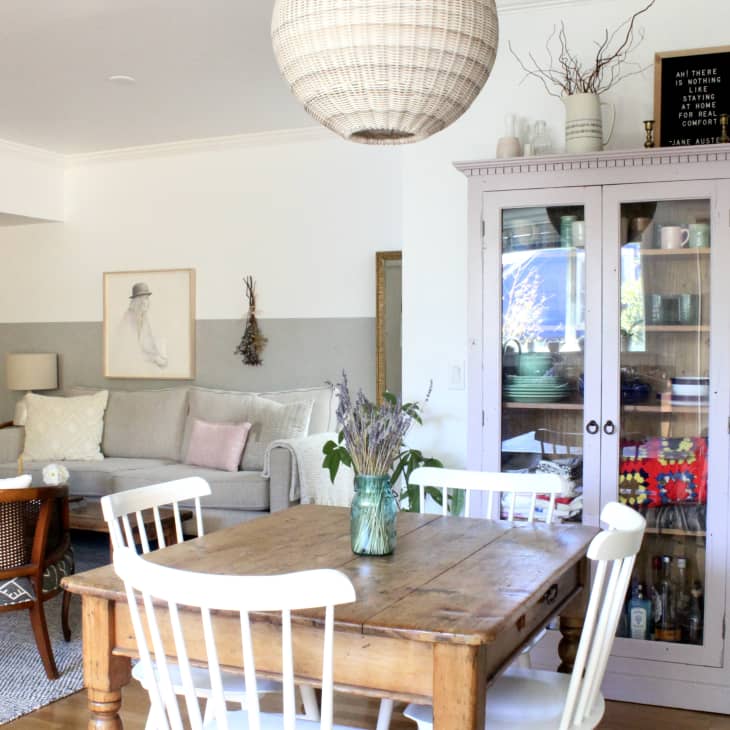 Dining area with wooden table, white chairs, glass cabinet, and cozy living room with a gray sofa and framed artwork.
