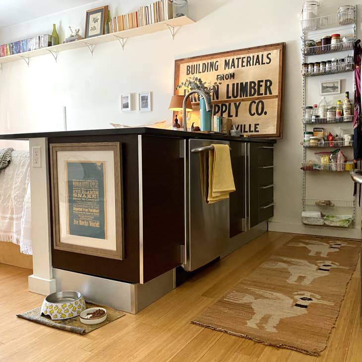 Kitchen with dark cabinets, vintage sign, open shelving, and a llama-patterned rug on wooden floor.