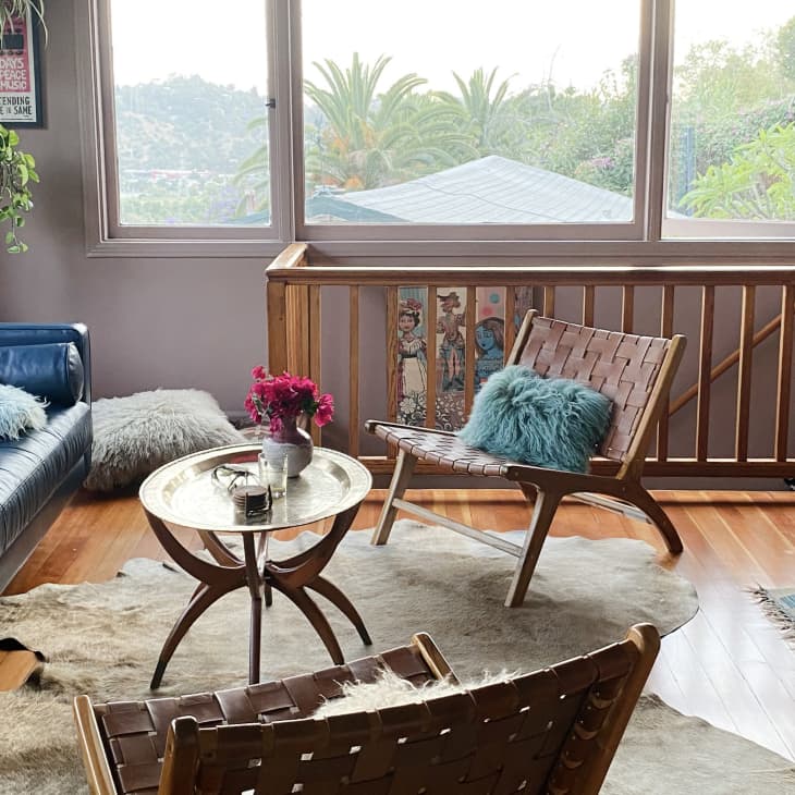 Cozy living room with blue sofa, woven chairs, fluffy pillows, round table, and large windows overlooking greenery.