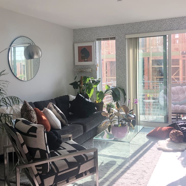 Modern living room with gray sectional sofa, glass coffee table, plants, and sliding glass doors leading to a balcony.