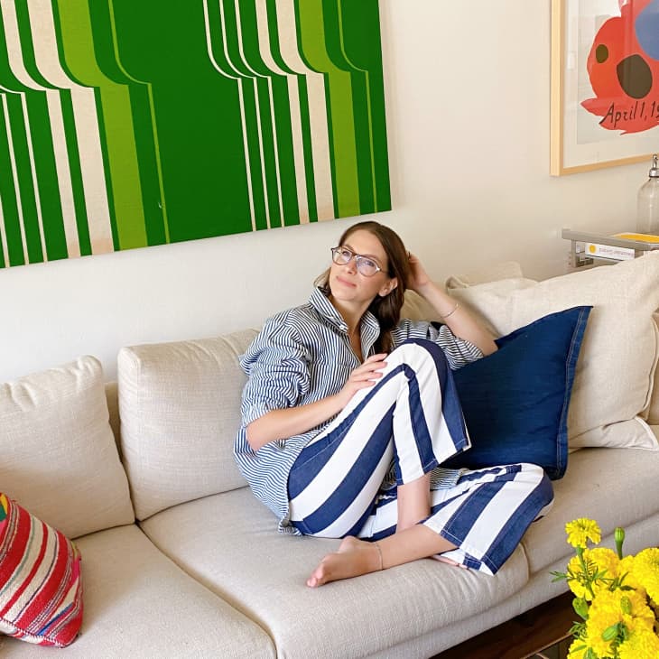 Woman in blue and white striped shorts sitting on a beige sofa with a green 1970s art piece hanging on the wall