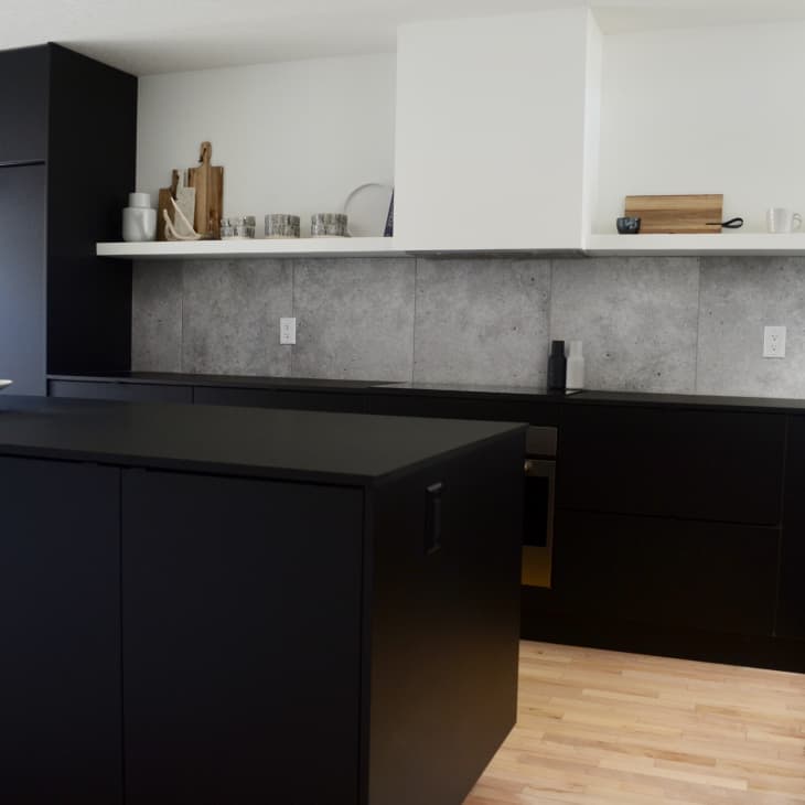 Streamlined kitchen with black cabinets, gray backsplash, and white shelving