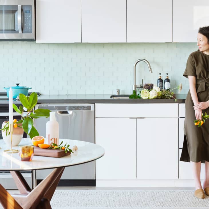 Woman in light, bright kitchen with subtle seafoam tile backsplash