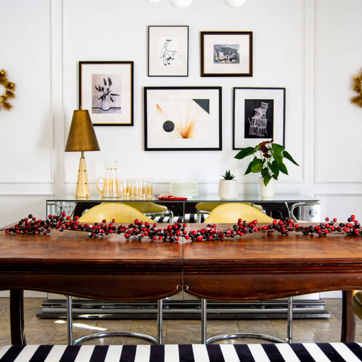 Dining room with wooden table, berry garland, yellow chairs, gold lamp, and framed art on white walls.