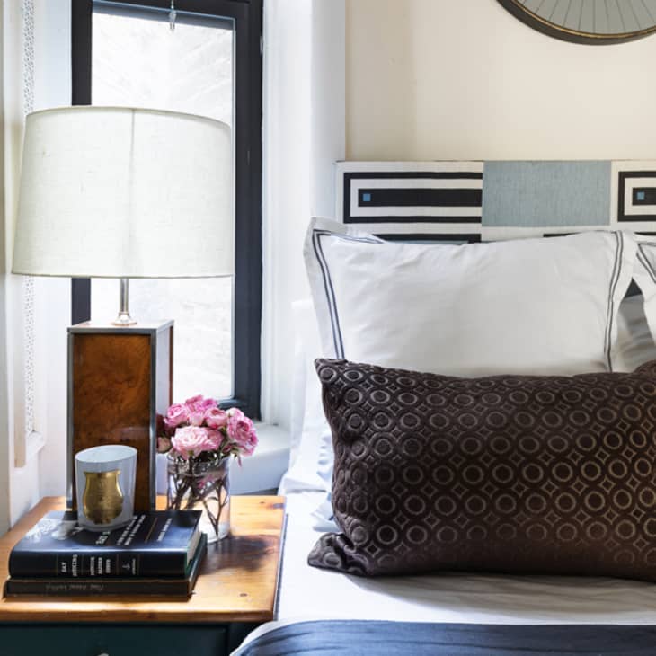 Corner of bed next to bedside table with brown lamp