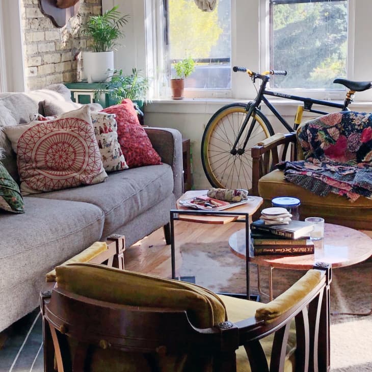 Cozy living room with a gray sofa, colorful pillows, a bicycle, and a chair with a patchwork quilt.